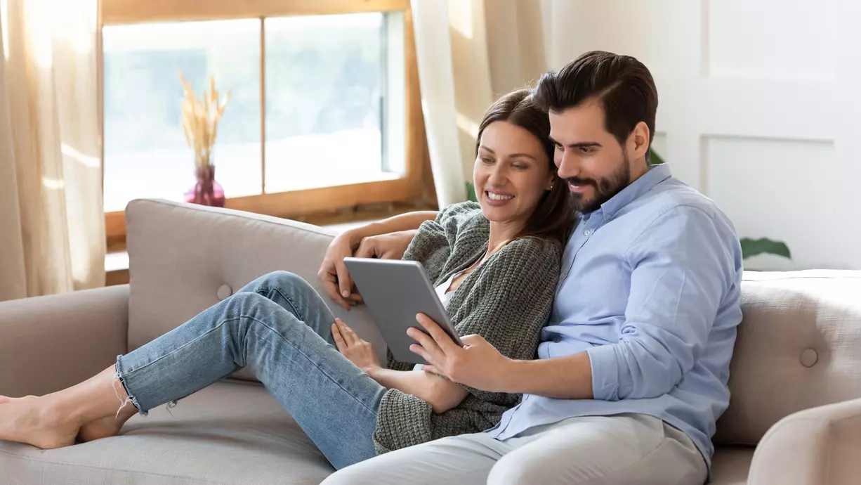 Casal sentado no sofá lendo no tablet